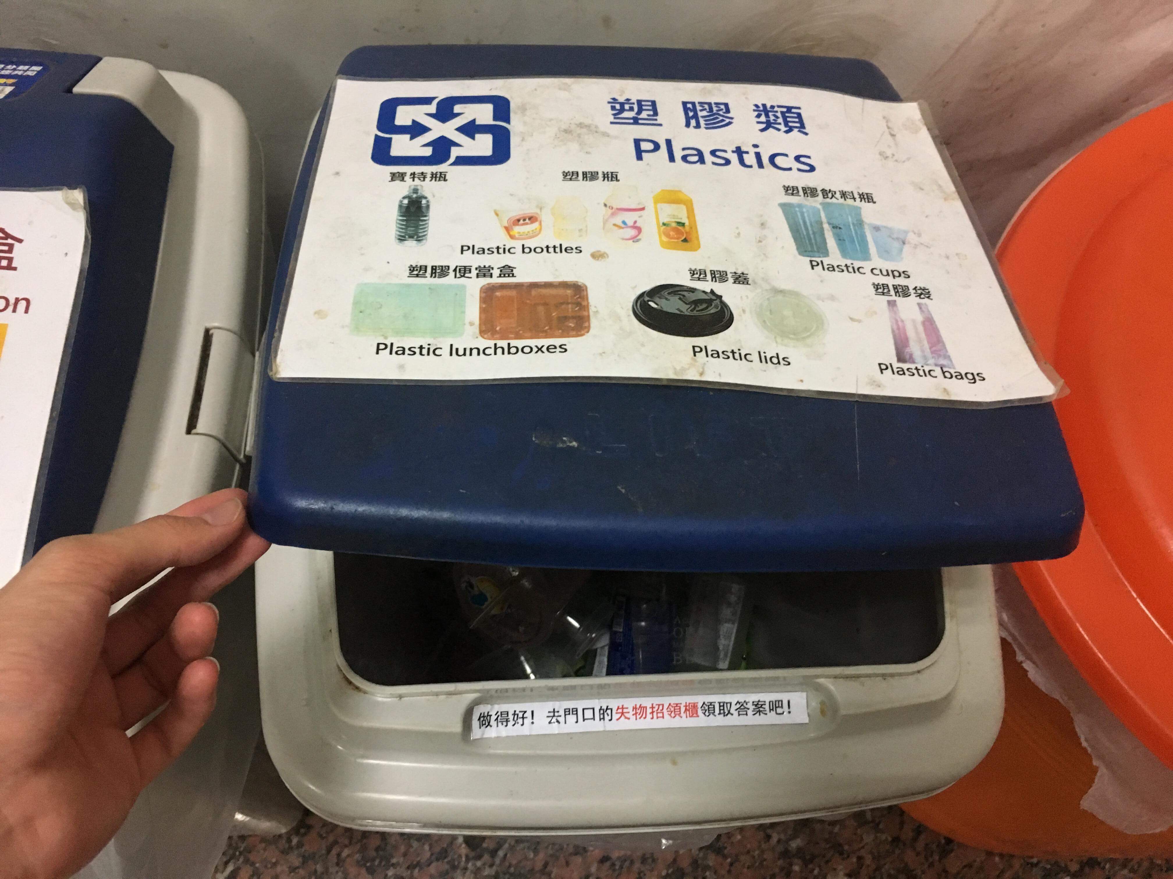 An arm that is holding the lid of a recycling bin.